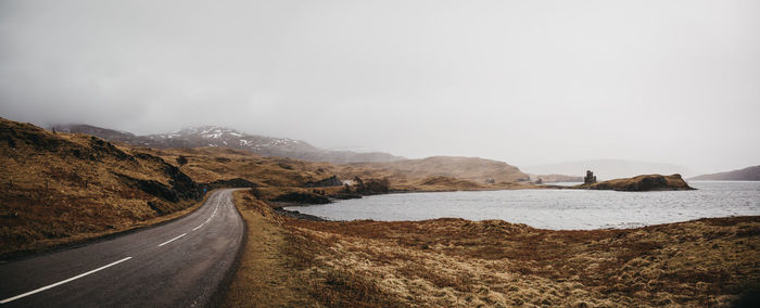 Country road leading towards mountains against sky during winter