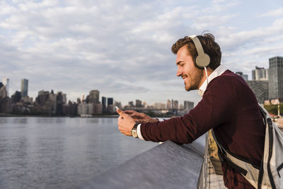 Usa, new york city, smiling young man with headphones and cell phone at east river