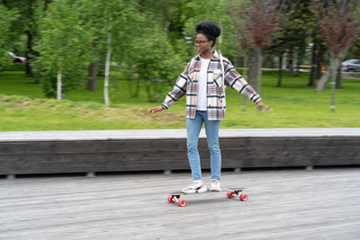 Active african american woman ride skateboard. trendy casual female skateboarding in urban city park