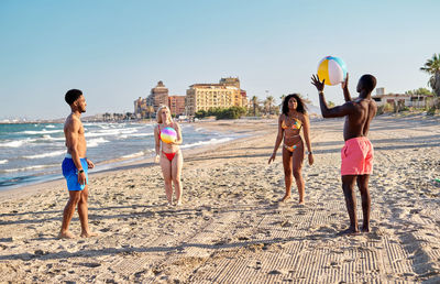 Multiethnic men and women playing beach ball on sandy beach near sea