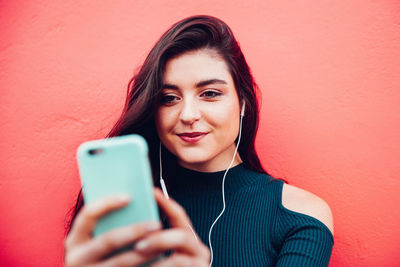 Young woman using smart phone against red wall