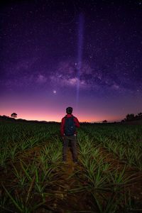 Rear view of man standing on field against sky at night