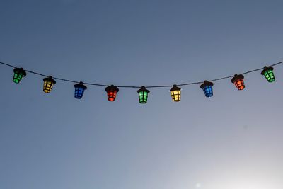 Low angle view of hanging lights against clear blue sky