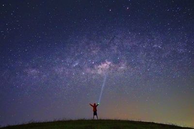 Rear view of man holding flash light while standing against star field at night