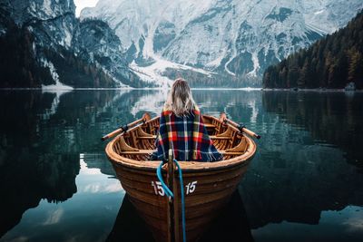 Rear view of woman sitting on boat in lake against mountains