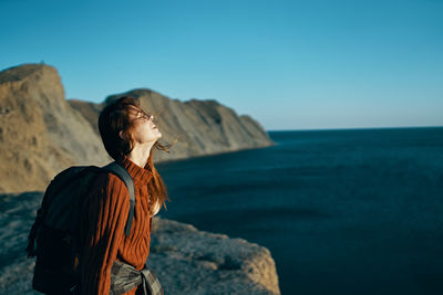 Man standing on rock by sea against clear sky