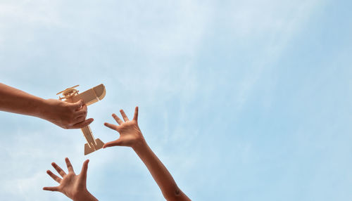 Low angle view of hand holding toy against sky