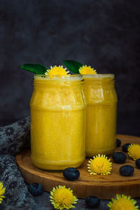 Yellow mango smoothies with flowers, berries, wooden plate on dark background. food and drink photo