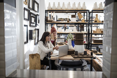 Two women with laptop in shop with shelf in background