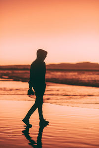 Silhouette woman walking at beach against sky during sunset