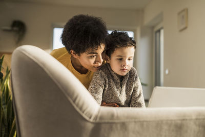 Young woman and boy using digital tablet while sitting on sofa at home