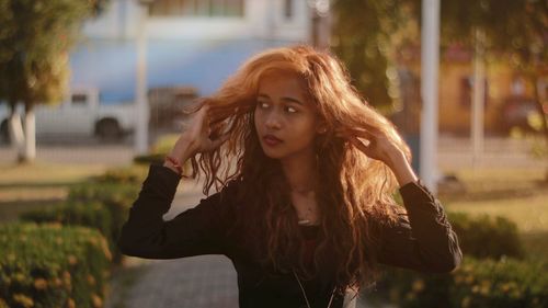 Young woman with hand in hair looking away while walking on footpath