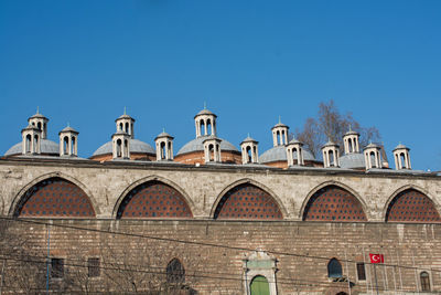 People by historic building against clear blue sky