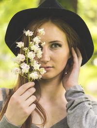 Portrait of young woman with long hair wearing hat holding flowers