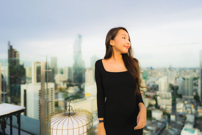 Young woman looking at cityscape against sky