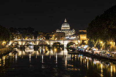 Illuminated bridge over river by buildings against sky
