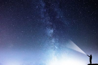 Man with flashlight standing against sky at night