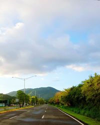 Empty road leading towards mountains against cloudy sky