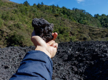 Man holding volcanic black porous stone or rock on active pacaya with recently dried black lava
