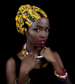 Close-up portrait of young woman in headwear against black background