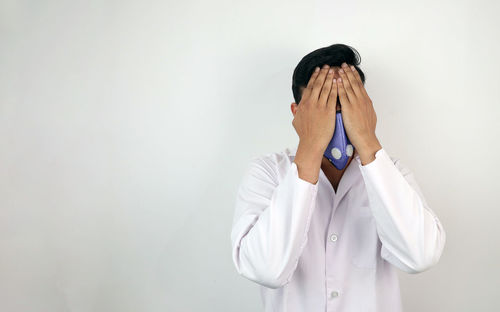 Midsection of man covering face against white wall