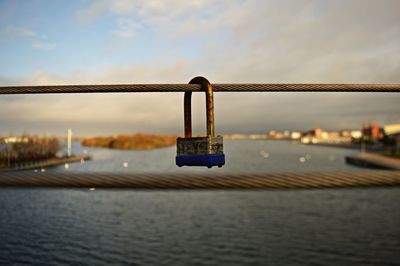 Padlocks on bridge over river against sky