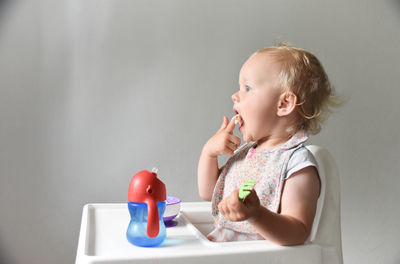 Almost 2 years old baby girl eating rice porridge with her hand. grey background