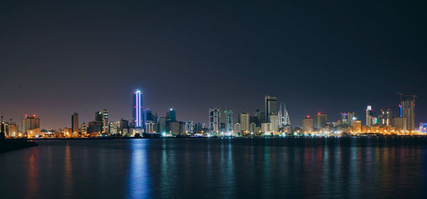 Sea by illuminated buildings against sky at night