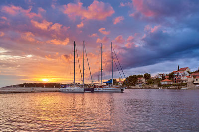 Sailboats moored in sea against sky during sunset