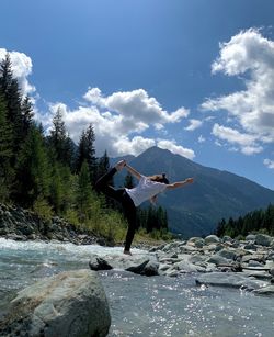 Rear view of man jumping on mountain against sky