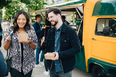 Female laughing while standing by male friend with box against food truck