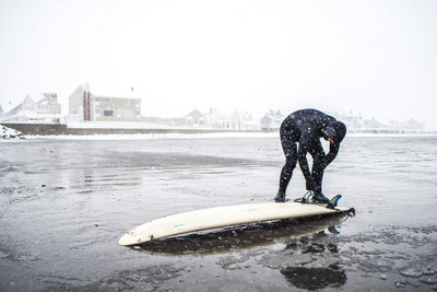 Surfer checking the bottom of board during a maine snow storm
