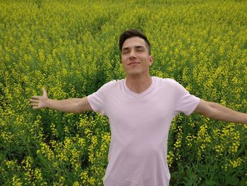 Smiling young man with eyes closed and arms outstretched standing against flowering plants at farm