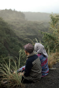 Rear view of couple sitting on the edge of cliff