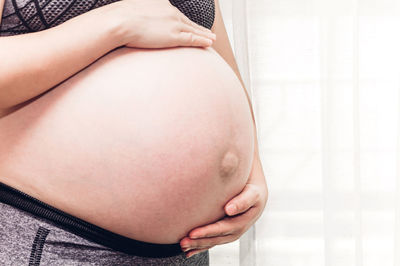 Midsection of pregnant woman with hands on stomach standing at home