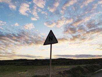 Road sign on field against cloudy sky during sunset