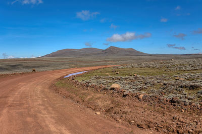 Dirt road on landscape against blue sky