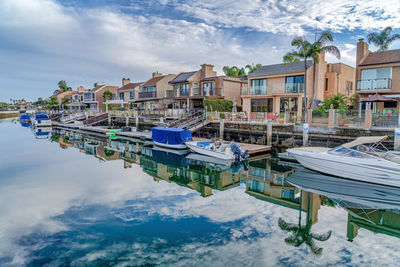 Boats moored on canal by houses against sky