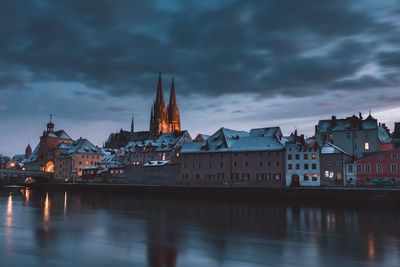 Buildings by river against cloudy sky