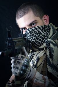 Close-up of man with shotgun standing against black background