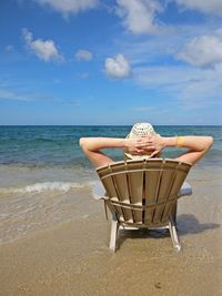 Rear view of woman sitting on chair at beach against sky