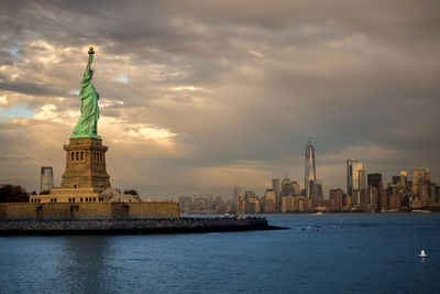 Statue of liberty with city skyline against cloudy sky