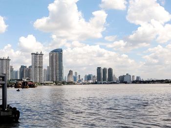 Sea by modern buildings against sky in city