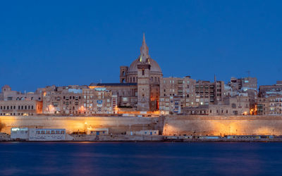 Illuminated buildings against blue sky at dusk