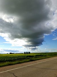 Road passing through field against cloudy sky