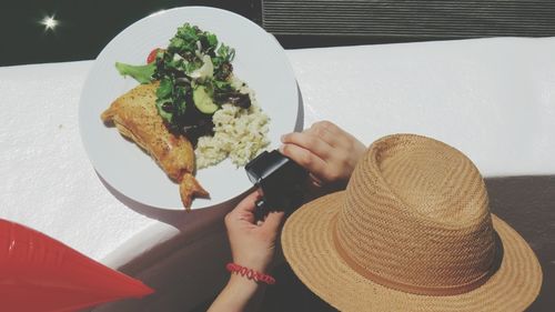 High angle view of woman wearing hat photographing food on retaining wall