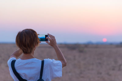 Rear view of mature woman photographing at sunset