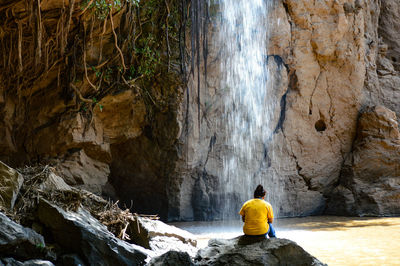 Rear view of man sitting on rock formation