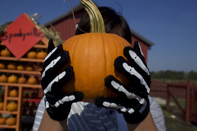 Midsection of woman holding pumpkin against orange during halloween