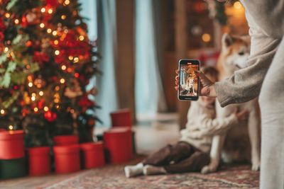 Candid authentic happy little boy in knitted beige sweater hugs dog with bow tie at home on xmas